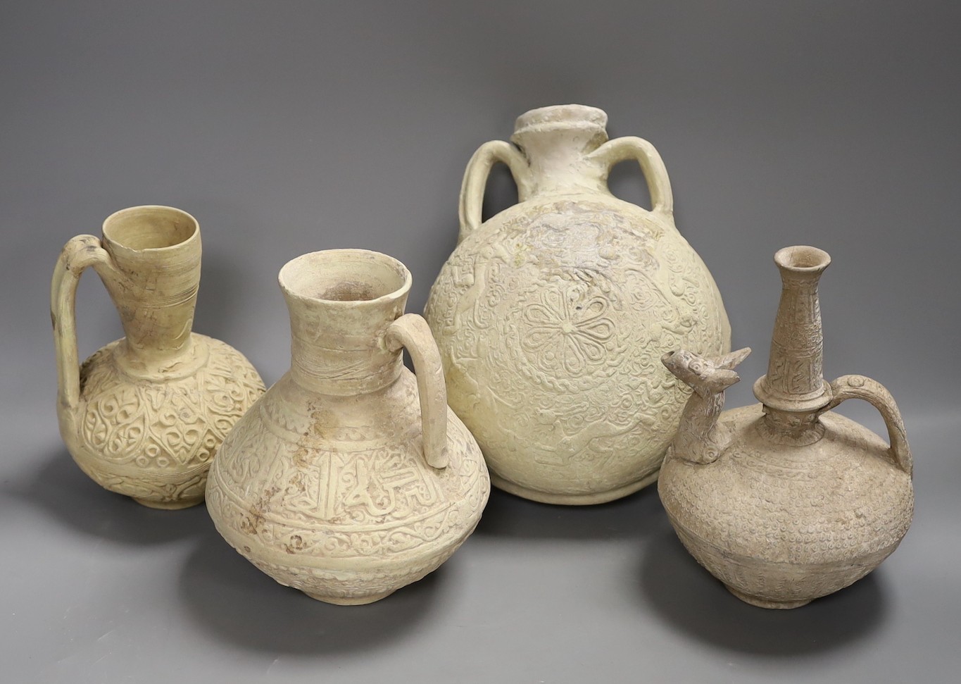 A group of Islamic terracotta vessels, Middle Eastern, possibly 12th century, including two jugs, an animal headed ewer and a two handled flask, The latter 25 cm high